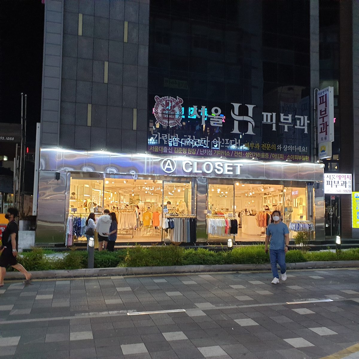 A mirrored-steel storefront lit at night with a bright shop floor behind glass